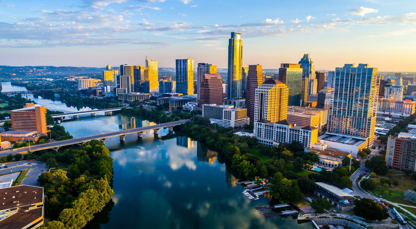 A vibrant cityscape at dusk with high-rise buildings reflected in a river, and multiple bridges crossing the water.