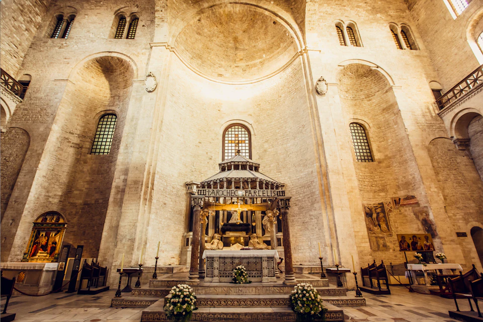 A large, ornate altar inside a cathedral with tall arched ceilings, stone walls, and flower arrangements at the base.