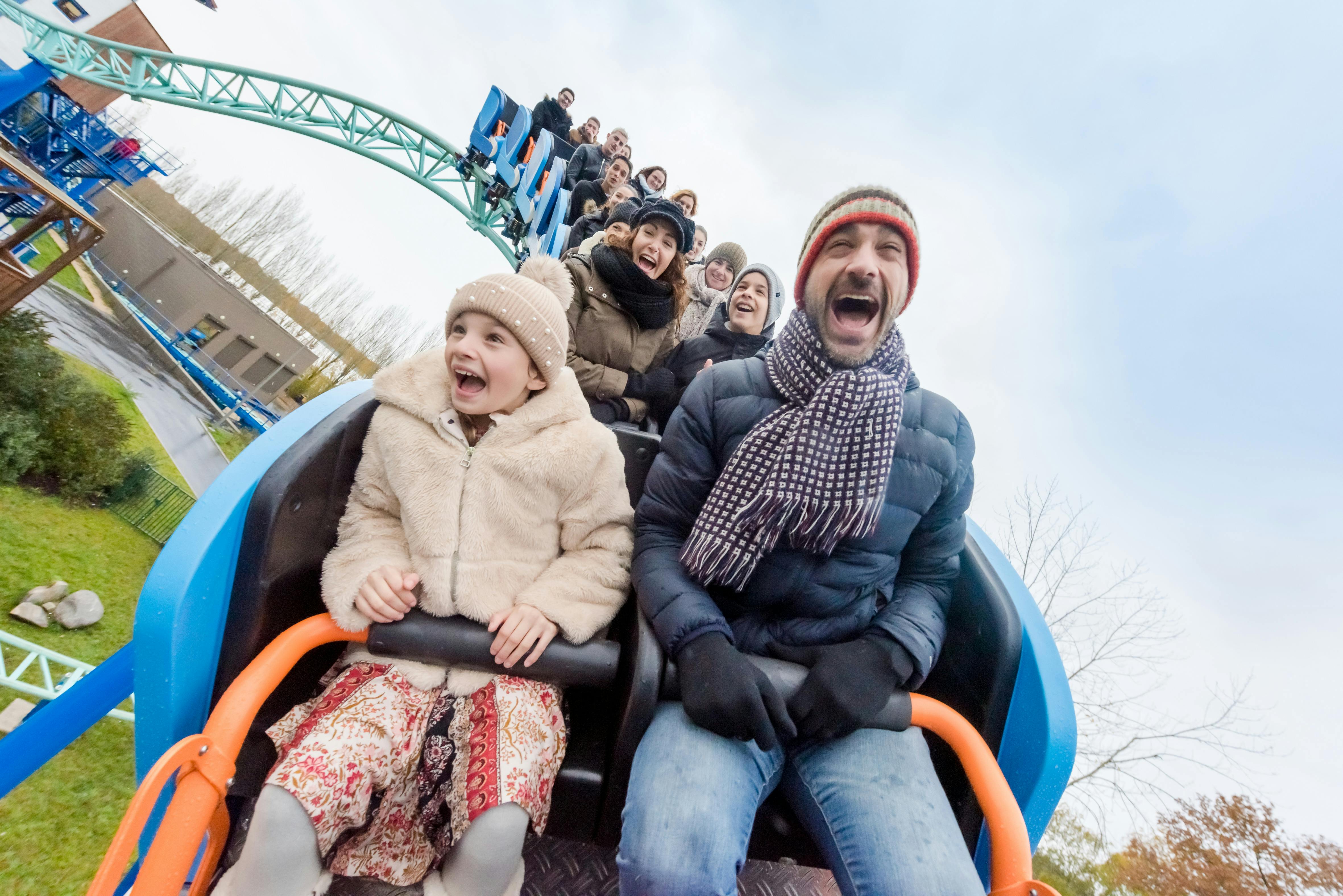 A group of people enjoying a rollercoaster ride, showing excitement and smiles. The background shows a track and sky.
