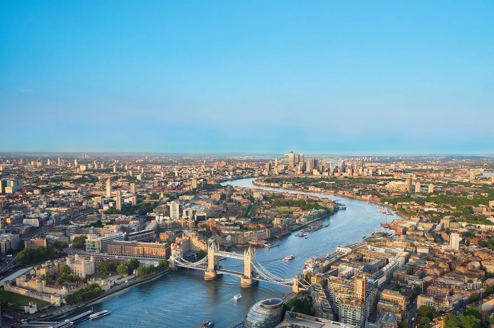 Aerial view of Tower Bridge spanning the River Thames in London, surrounded by city buildings and a clear blue sky.