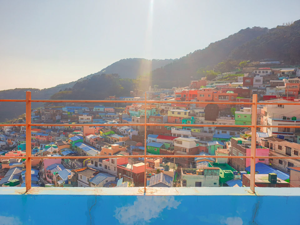 A vibrant hillside village with colorful buildings under a clear sky, viewed from a balcony with railings.