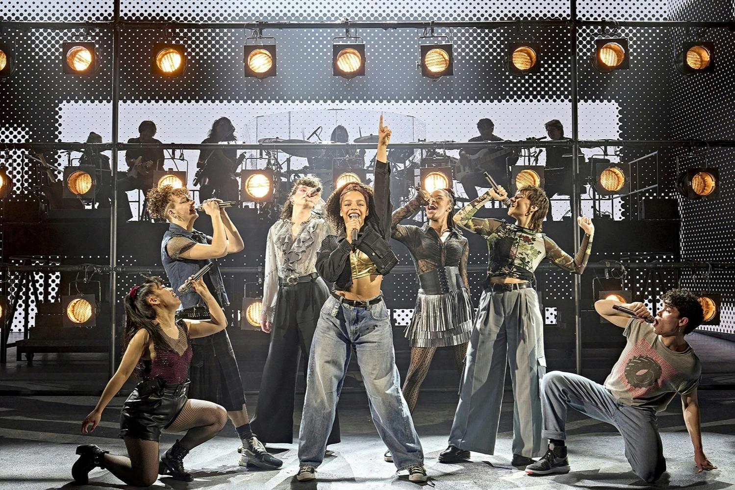 一群表演者在舞台上唱歌和跳舞，在灯火通明的背景下，音乐家呈现轮廓。