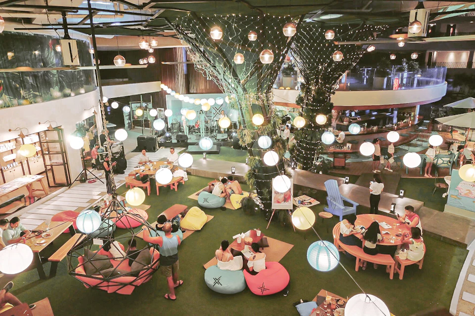 People enjoying a cozy indoor setting with bean bags, tables, and hanging string lights, creating a festive atmosphere.