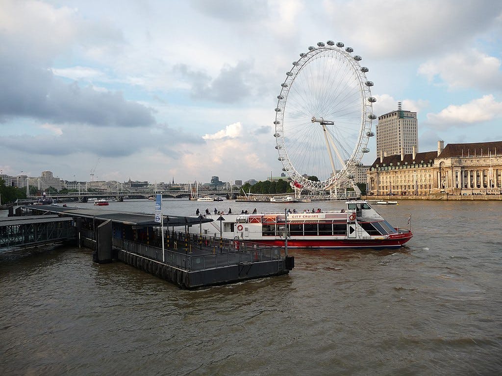 Een aangemeerde rondvaartboot op de rivier de Theems met de London Eye en historische gebouwen op de achtergrond.