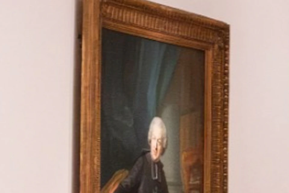 A couple holding hands walking through an art gallery with framed paintings on white walls and wooden floors.