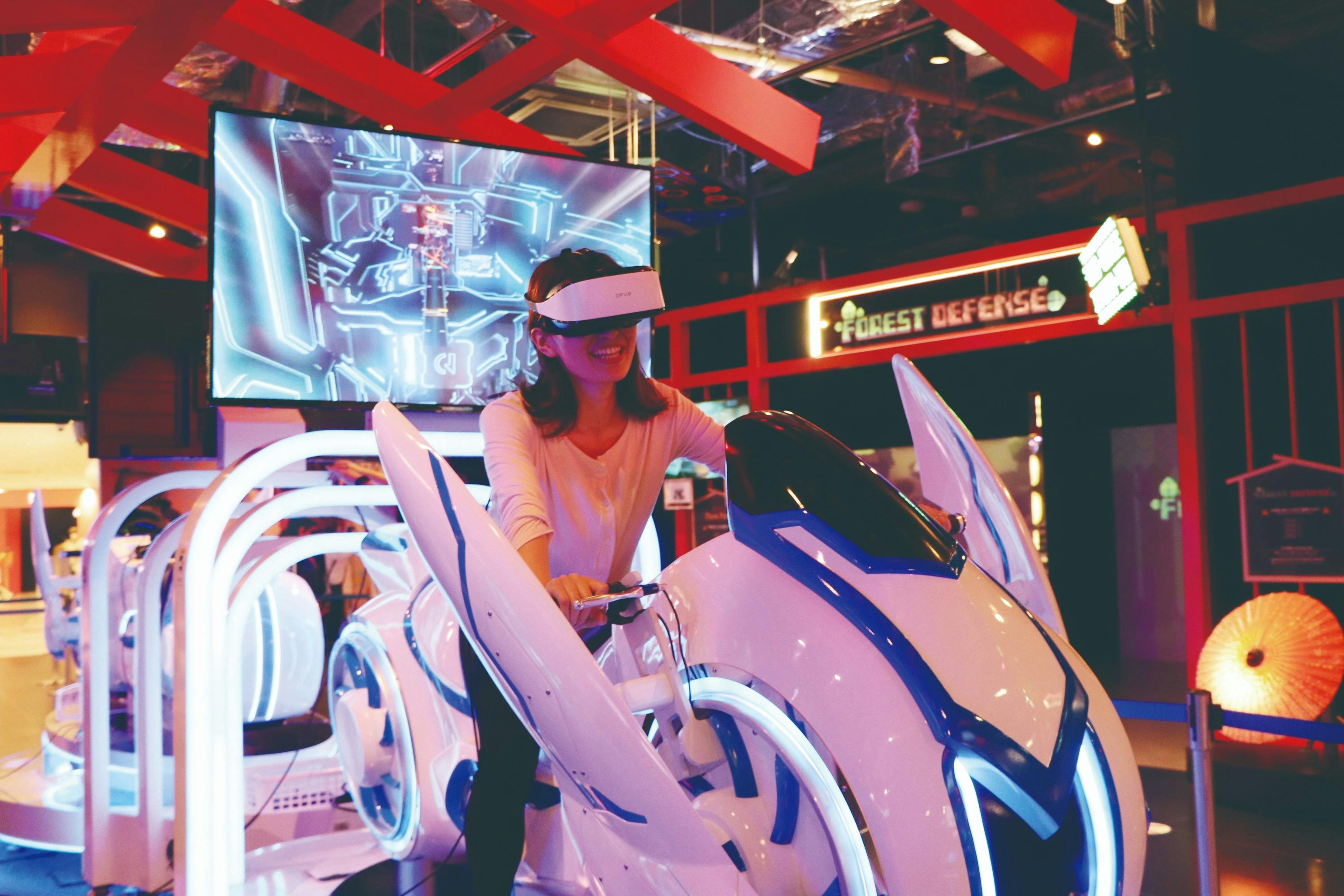Une personne portant un casque de réalité virtuelle et pilotant un simulateur de moto futuriste dans une salle d'arcade.