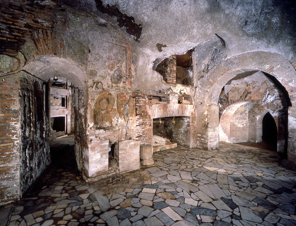 Ancient stone room with arched doorways, frescoed walls, and a tiled floor, featuring worn and weathered surfaces.