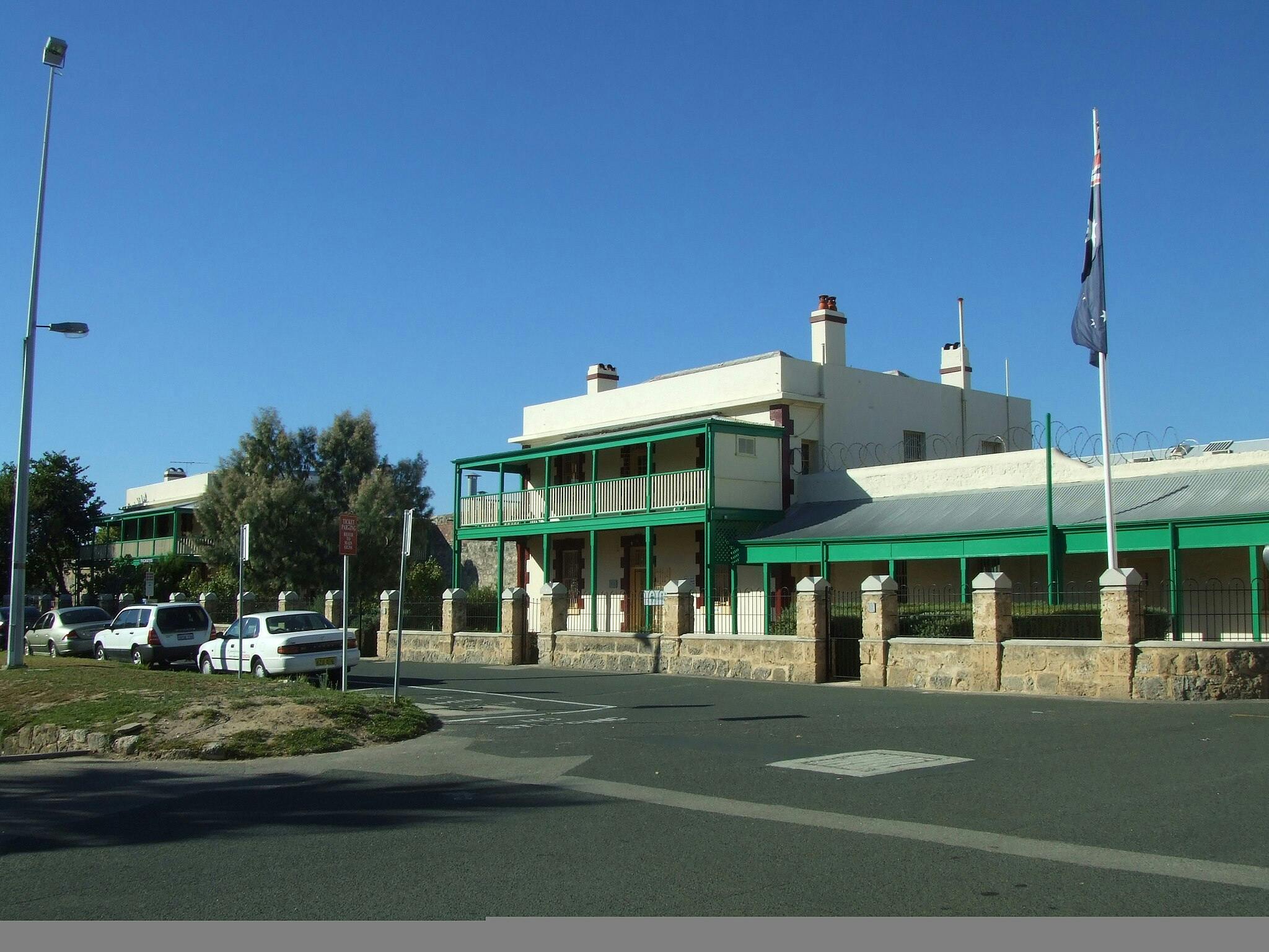 햇살이 내리쬐는 거리에 녹색 악센트가 있는 건물, 깃대, 주차된 차량이 있습니다. 푸르름과 맑고 푸른 하늘을 배경으로.