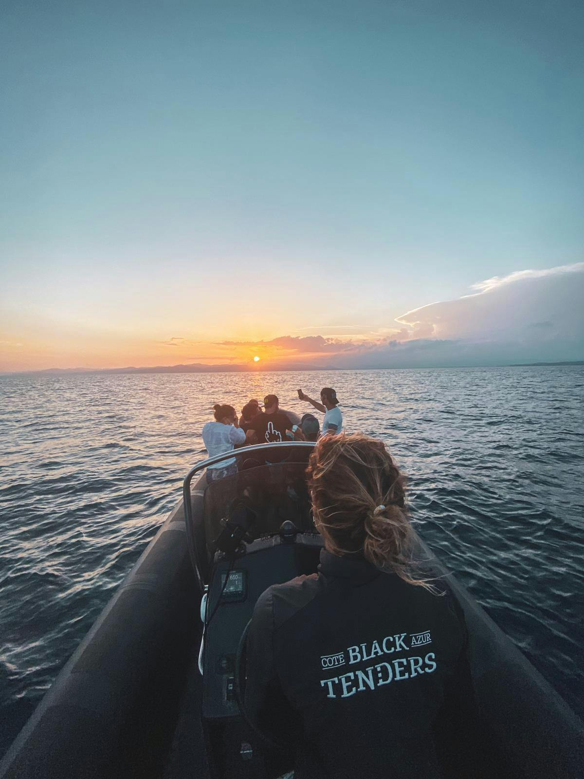 一群人在船上观看海上的日落，前景中有一个人穿着“黑蓝色招标”夹克。