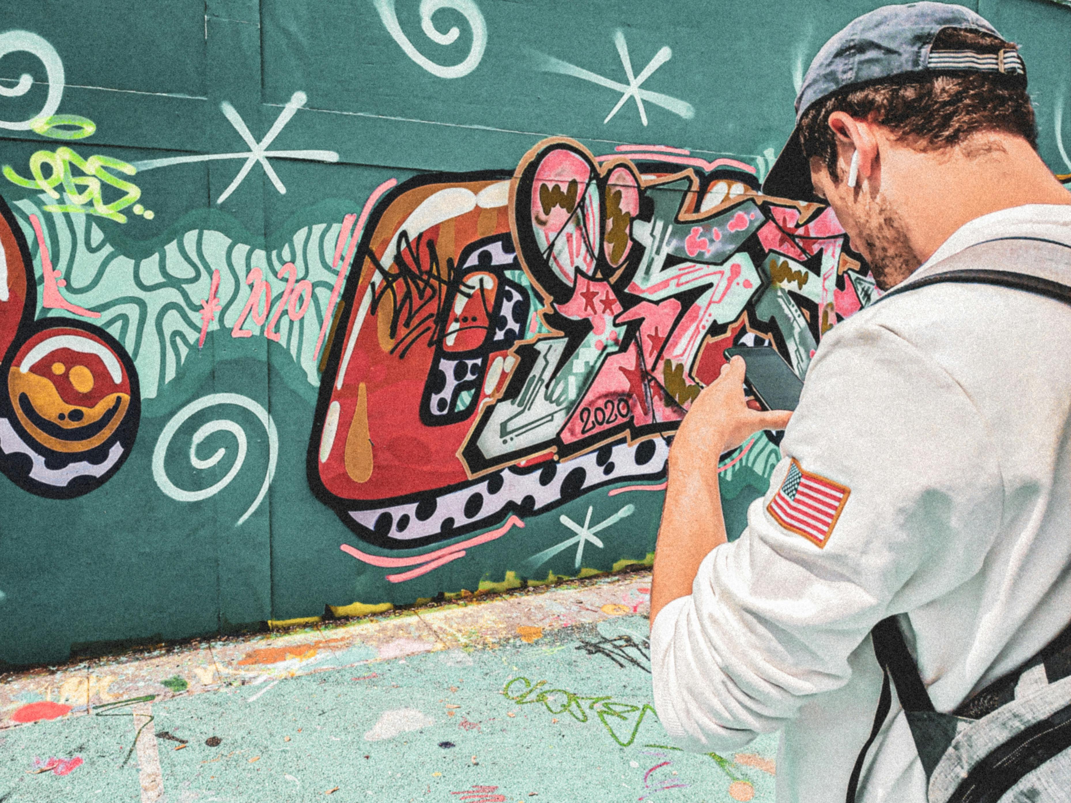 穿着白色夹克的男士，身上挂着美国国旗徽章，在绿色墙壁上拍摄彩色涂鸦。