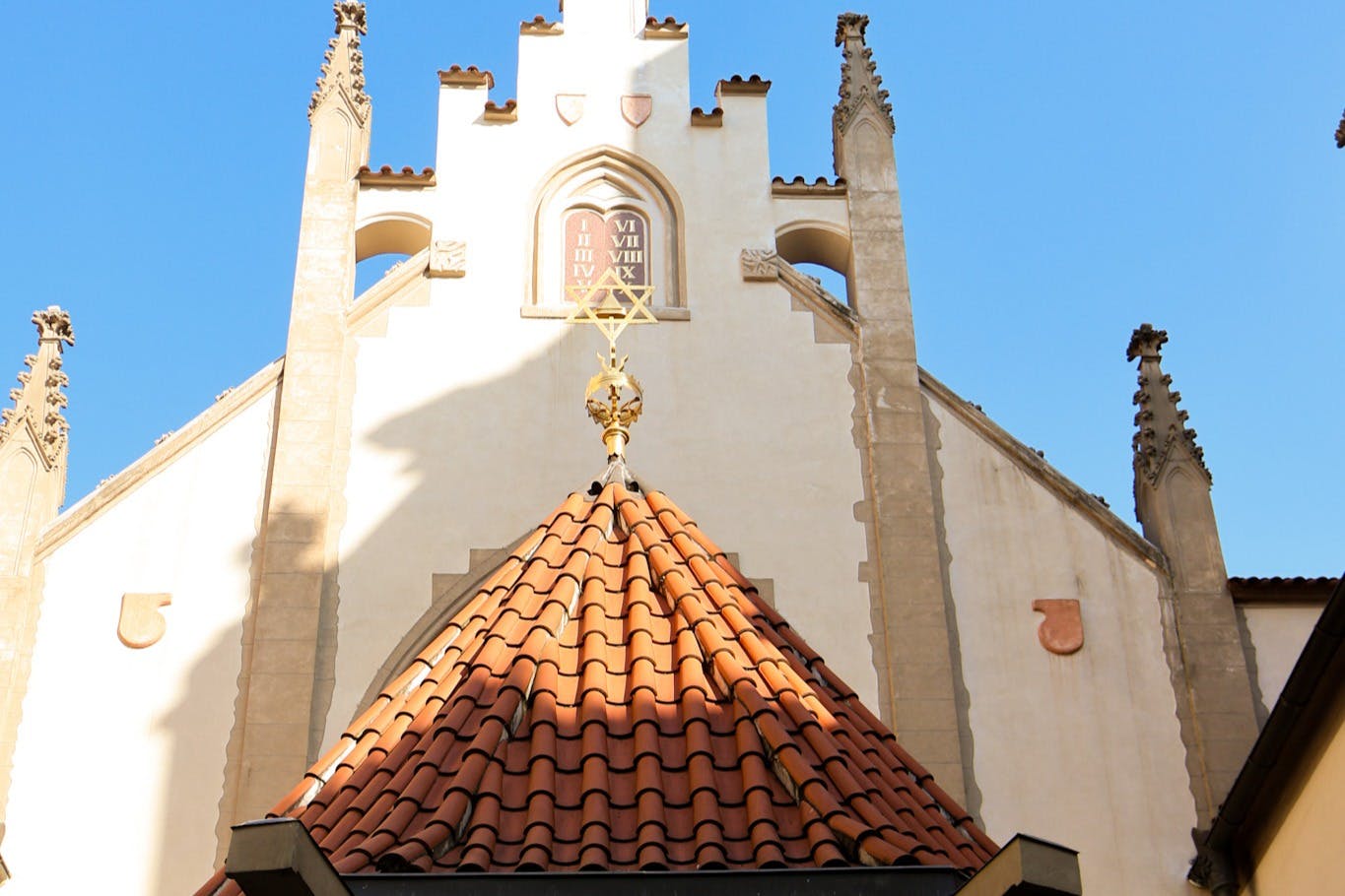 빨간색 타일로 마감된 지붕, 화려한 디테일, 맑고 푸른 하늘 아래 정면의 시계가 있는 유서 깊은 건물입니다.
