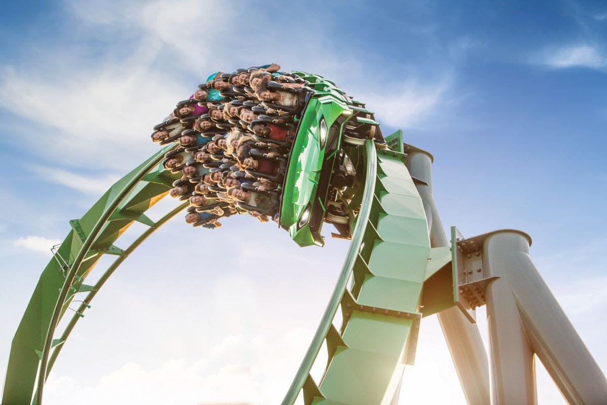 Persone che salgono su un ottovolante verde, a testa in giù su un anello, con un cielo azzurro sullo sfondo.