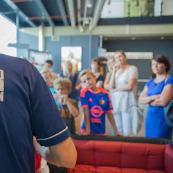 En man med ”Feyenoord Museum Rondleidingen” på skjortan leder en rundtur med uppmärksamma barn och vuxna i bakgrunden.