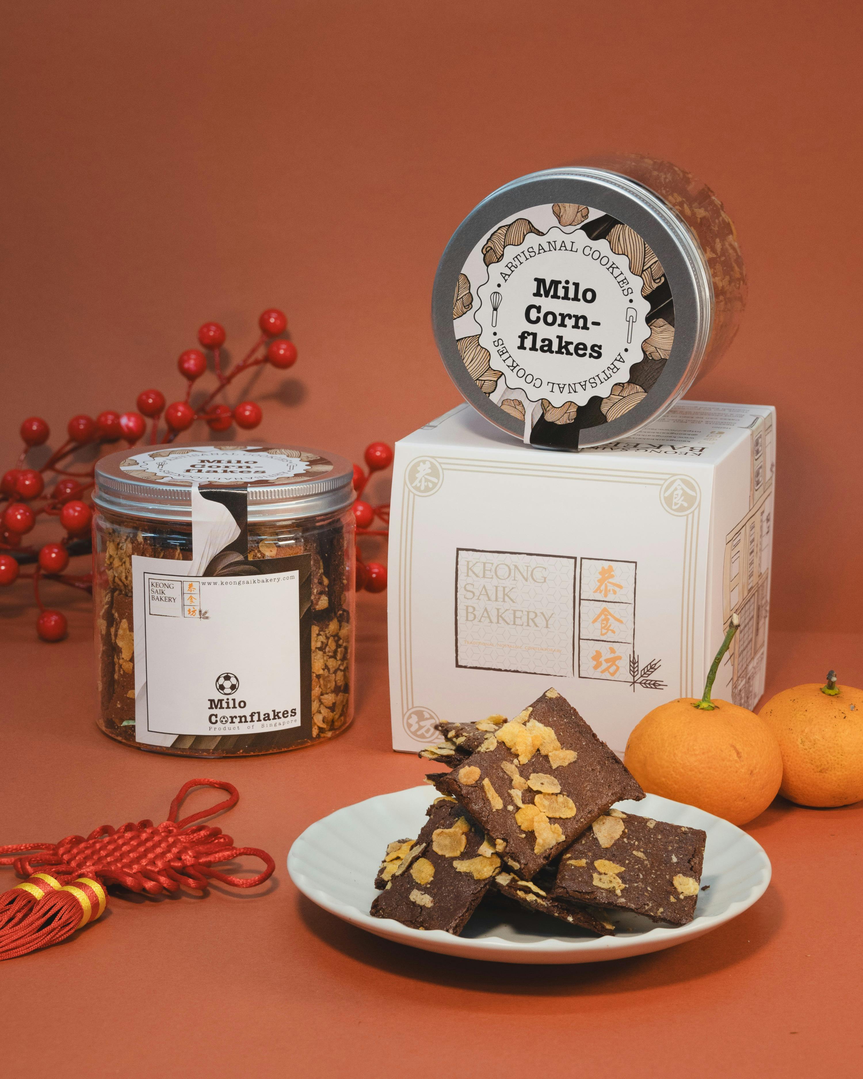 A display of Milo Cornflakes cookies in jars and a plate of brownies with cornflakes, decorated with tangerines and red ornaments.