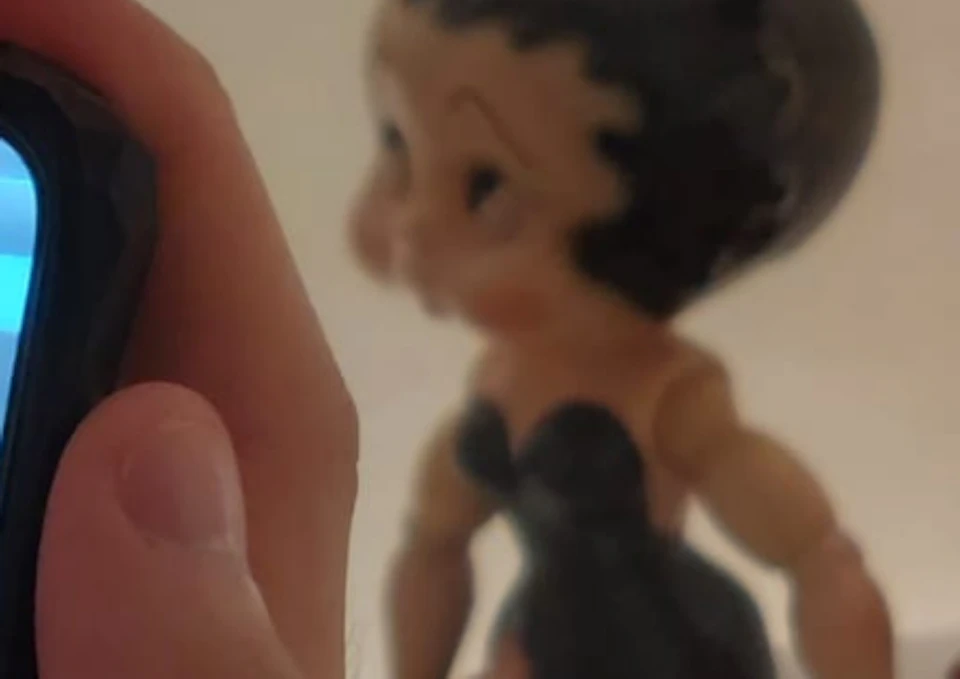 A hand holding a smartphone displaying an augmented reality image of Betty Boop dolls, with two real Betty Boop dolls in the background.