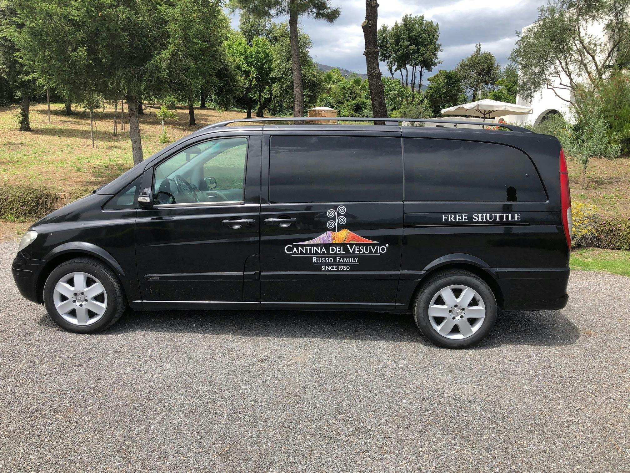 一辆标有“Cantina del Vesuvio”的黑色面包车，停在砾石路上，后面有树木和绿植。