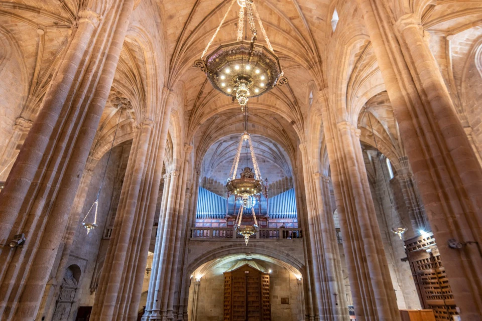 Interior of a grand cathedral with vaulted ceilings, ornate chandeliers, and a large pipe organ at the back.