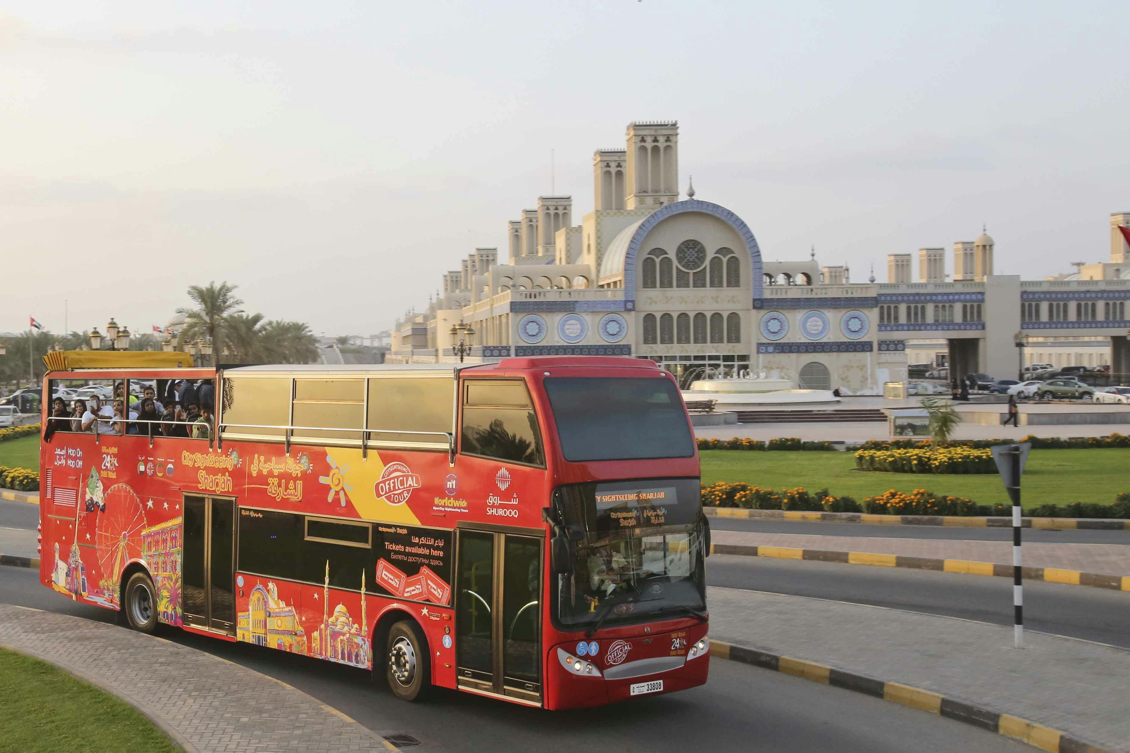 A red double-decker tour bus passing a large building with intricate blue and white detailing and multiple towers.