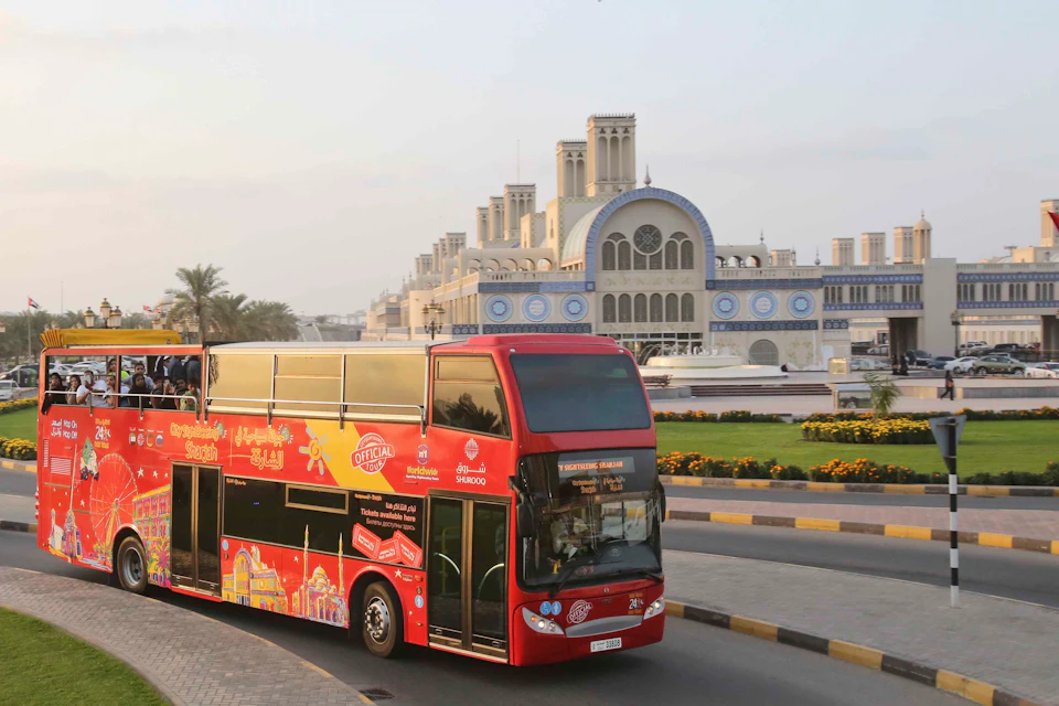 A red double-decker tour bus passing a large building with intricate blue and white detailing and multiple towers.