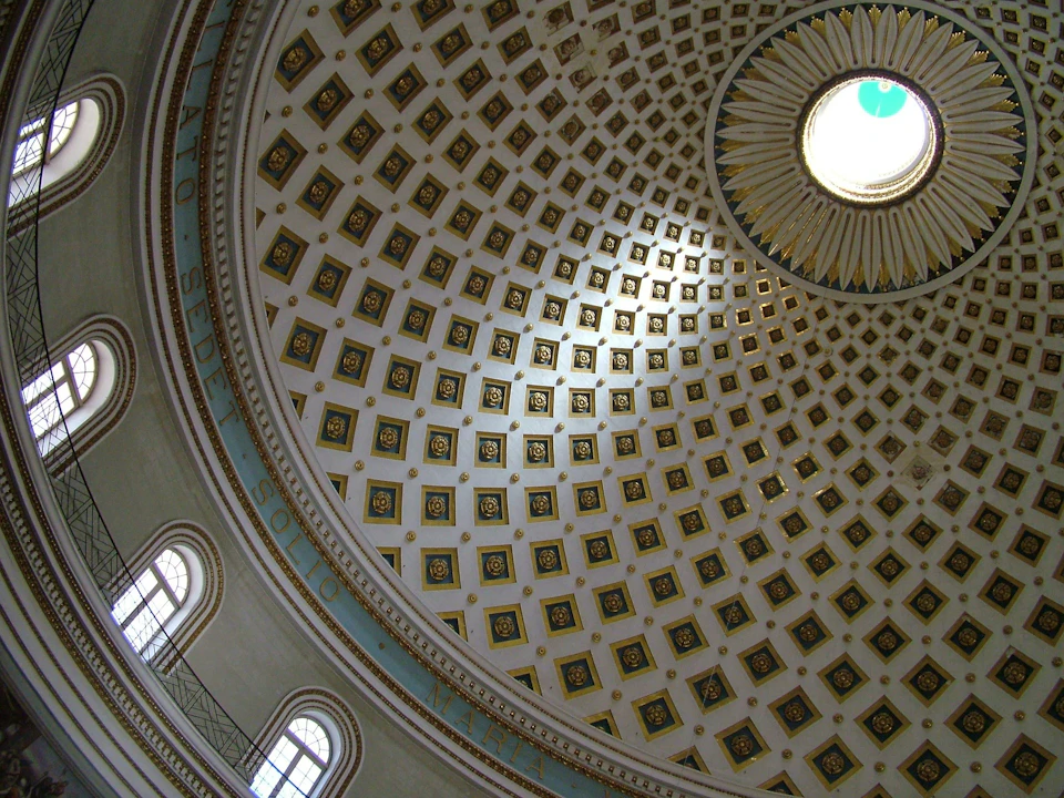 Ornate dome interior with square decorative patterns and a central skylight. Arched windows are visible at the lower edge.