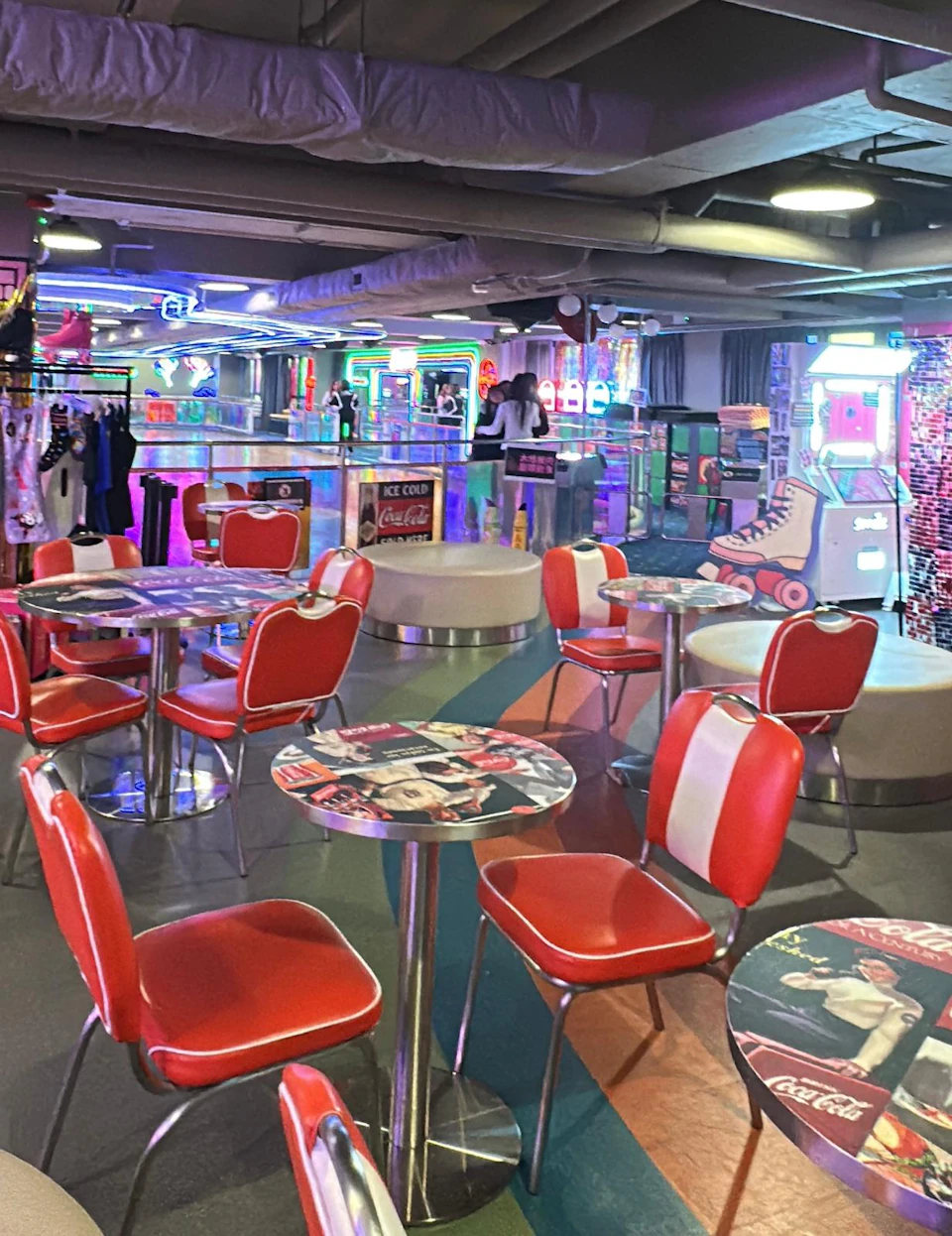Retro-themed diner with red chairs, vintage-style tables, neon lights, and a colorful roller skating decor.