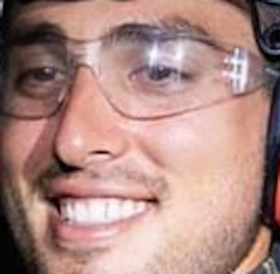 A person wearing outdoor gear and a headlamp smiles while holding a small reptile at night.