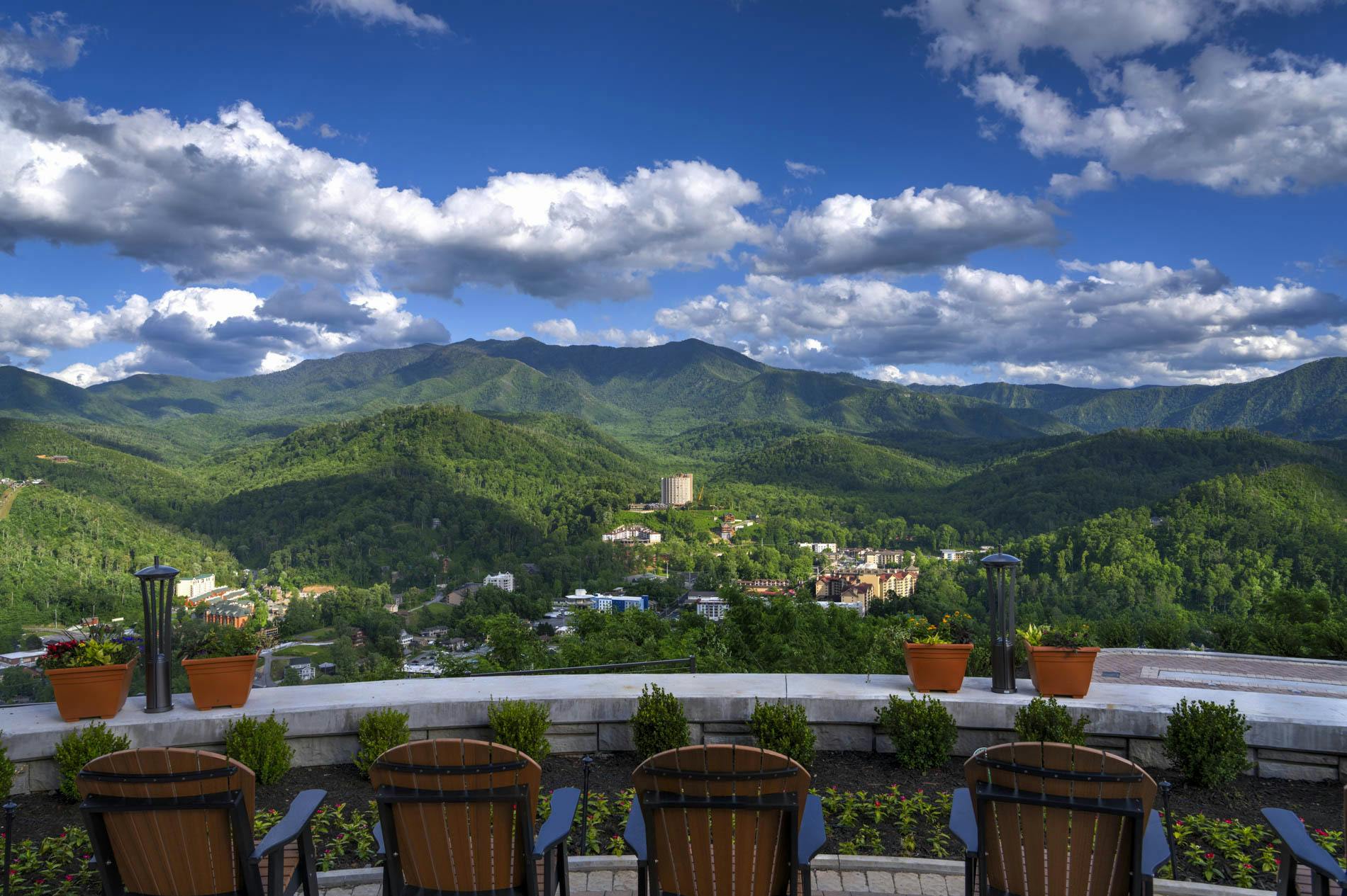 Dřevěné židle s malebným výhledem na svěží zelené hory a částečně zataženou oblohu s budovami roztroušenými v údolí.