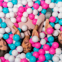 Tre personer som ler och skrattar, nedsänkta i rosa, blå och vita plastkulor.