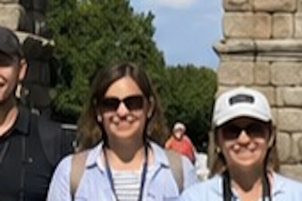 A group of people posing in front of an ancient stone aqueduct under a clear blue sky.