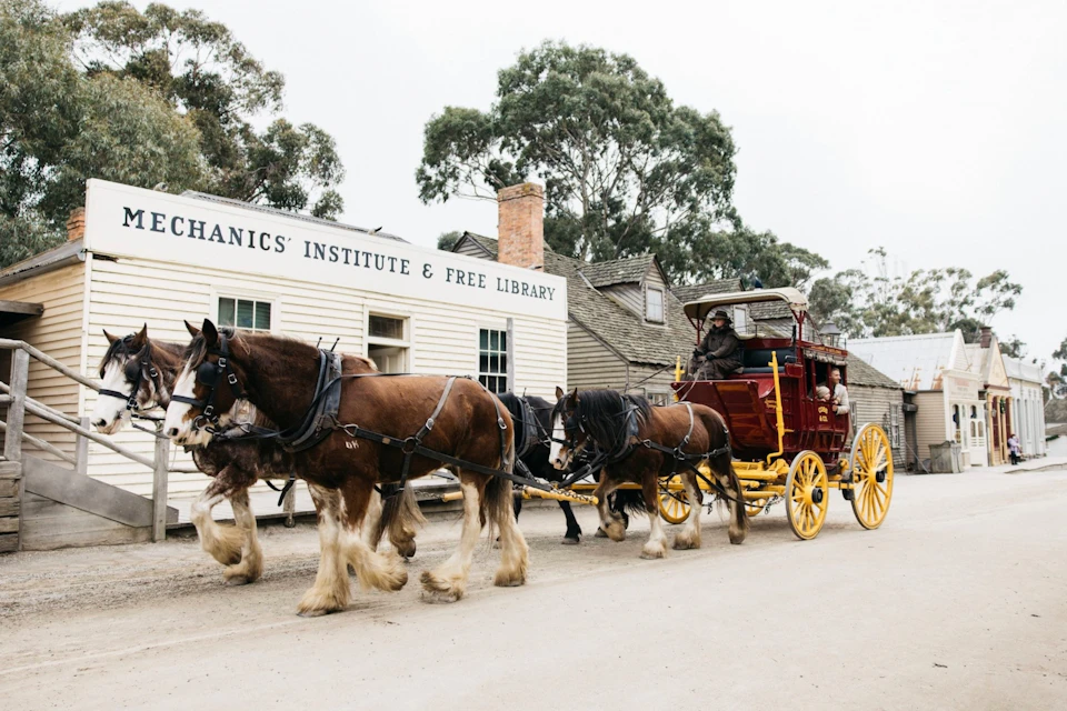 A horse-drawn carriage with yellow wheels in front of a vintage building labeled 'Mechanics' Institute & Free Library.'