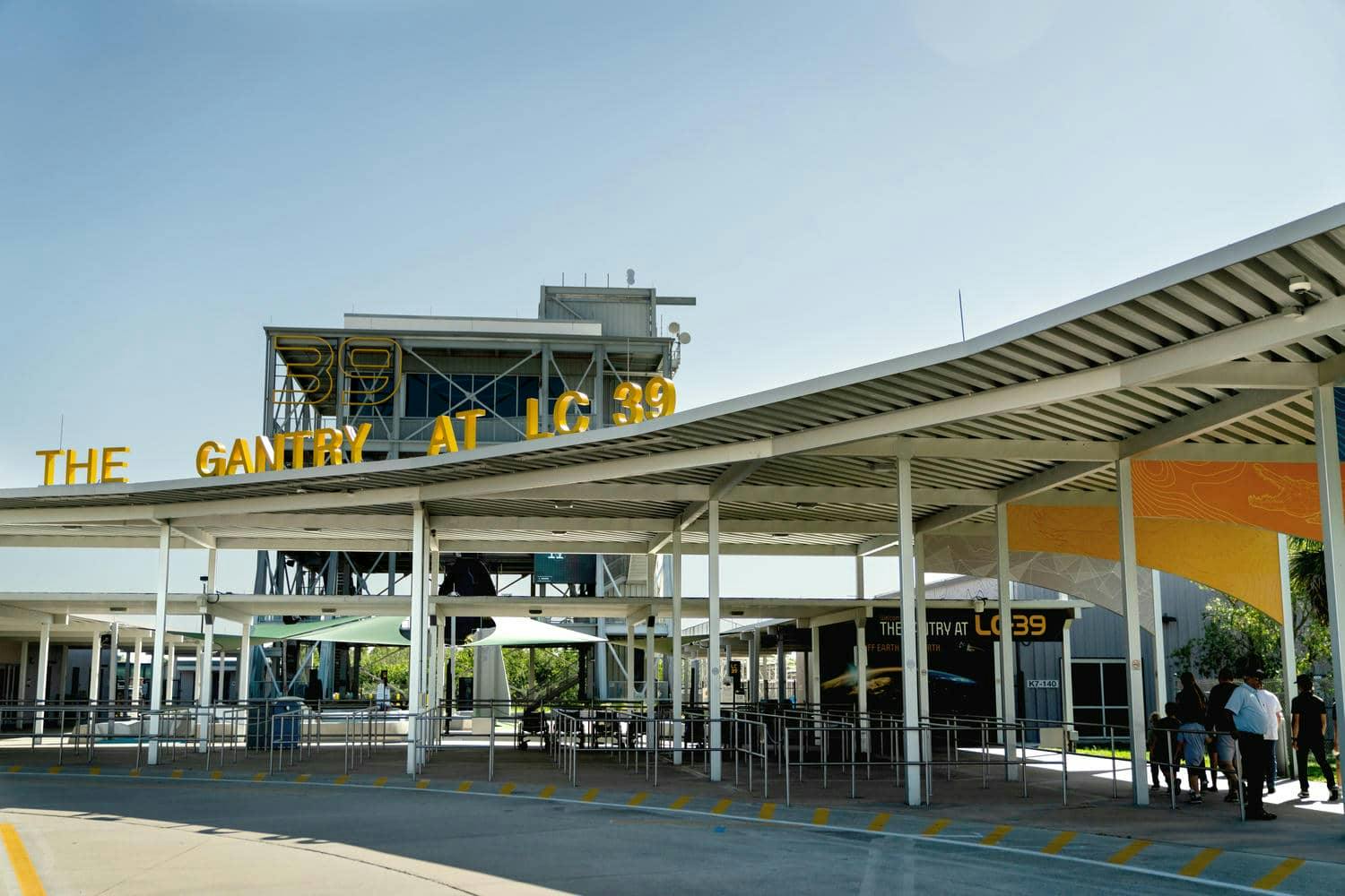 Outdoor exhibit area with a covered pathway and signs reading "The Gantry at LC 39." Turnstiles and an entrance structure visible.