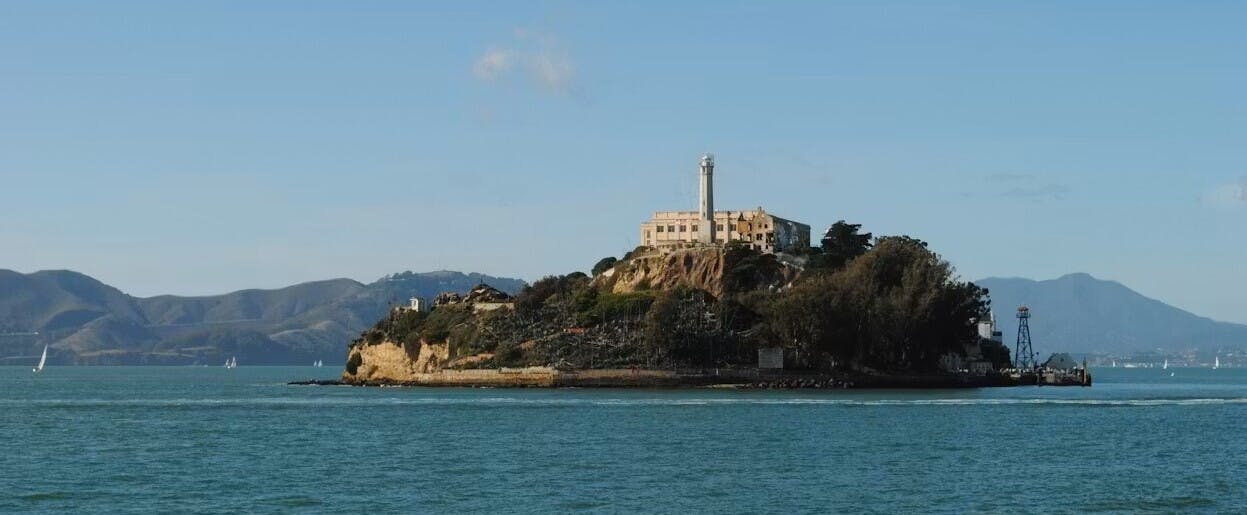 一座风化的灯塔和周围的建筑坐落在晴朗的蓝天下的悬崖上。