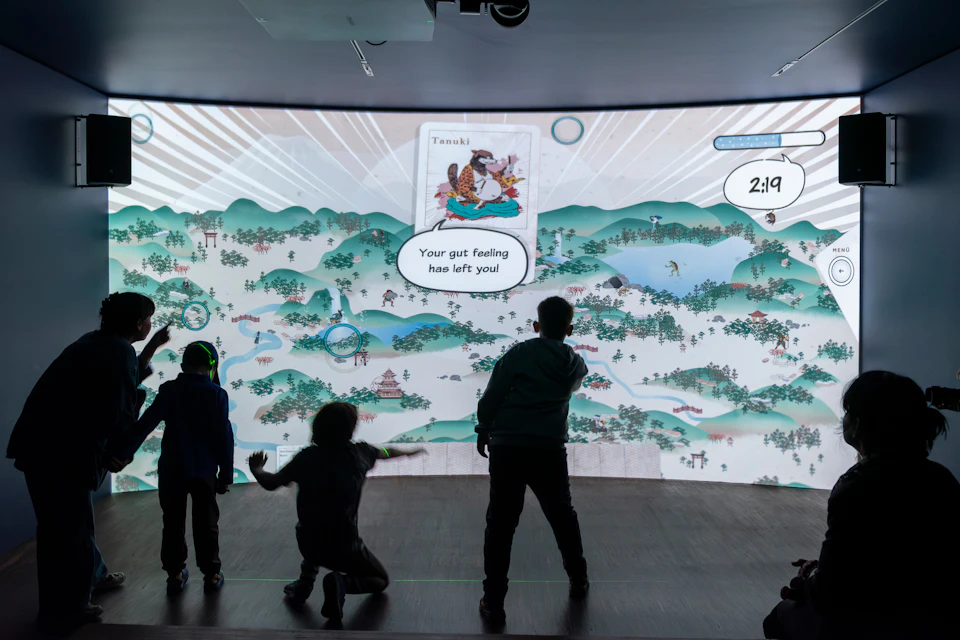 A group of children interacting with a large digital display showing a colourful animated landscape and messages.