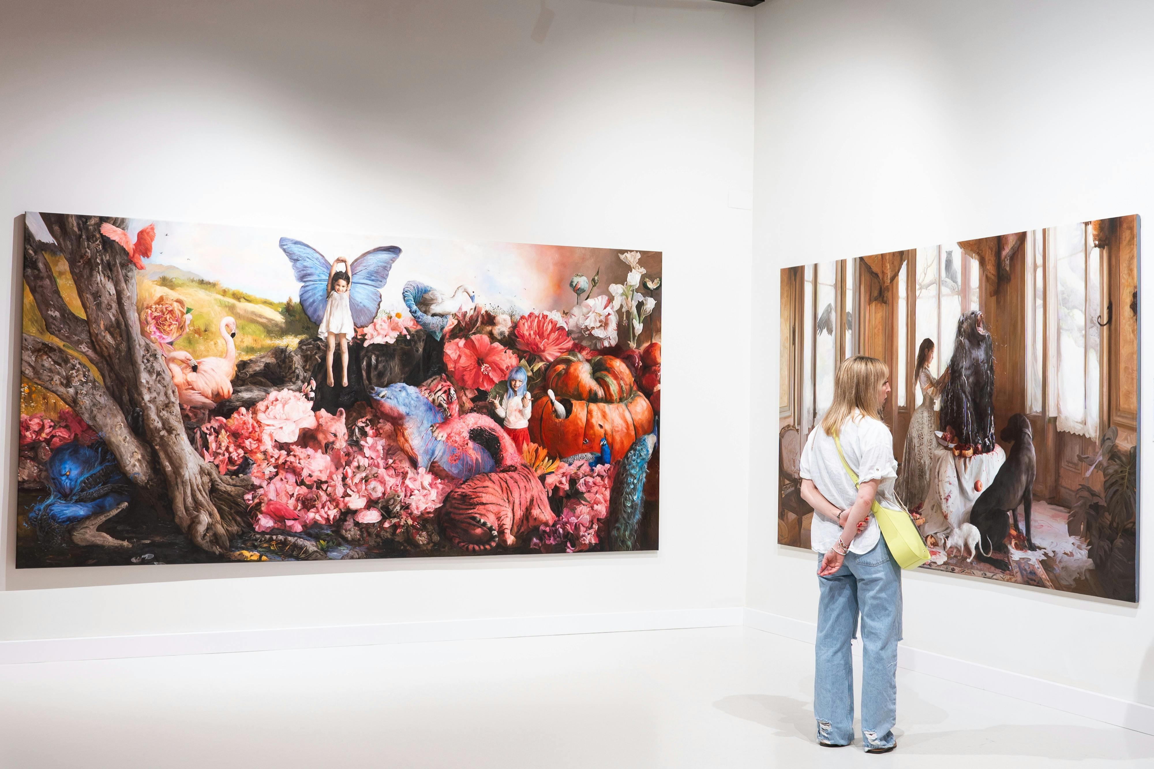 한 사람이 미술관에 전시된 다채로운 그림을 관찰하며 초현실적이고 자연에서 영감을 받은 작품을 감상합니다.