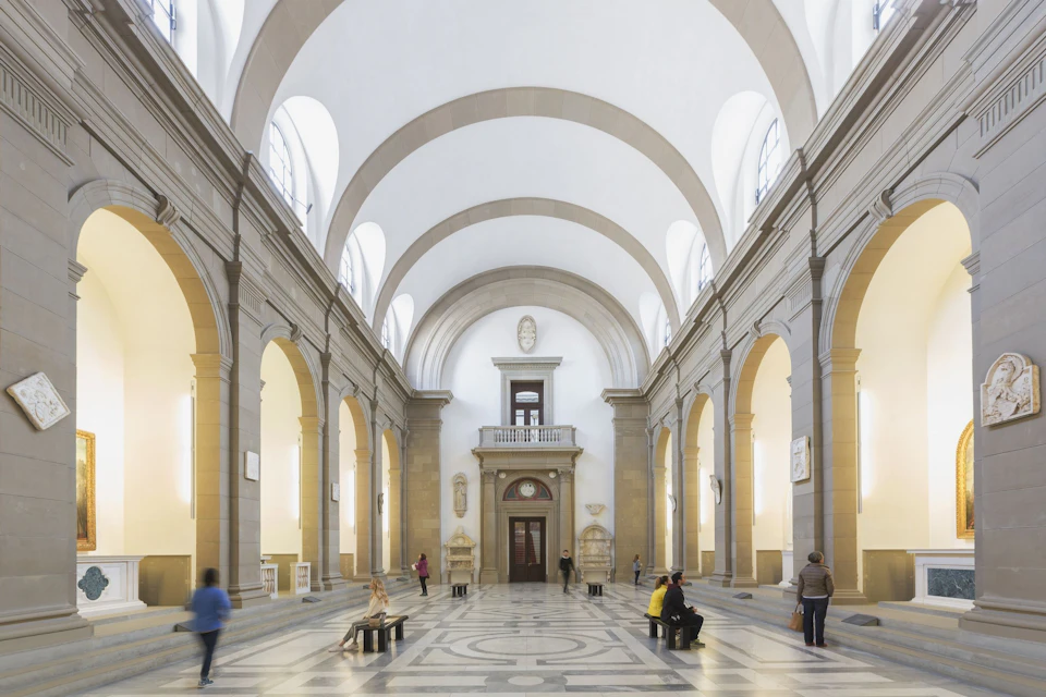A spacious hall with high arched ceilings, decorative columns, and people walking or sitting on benches.