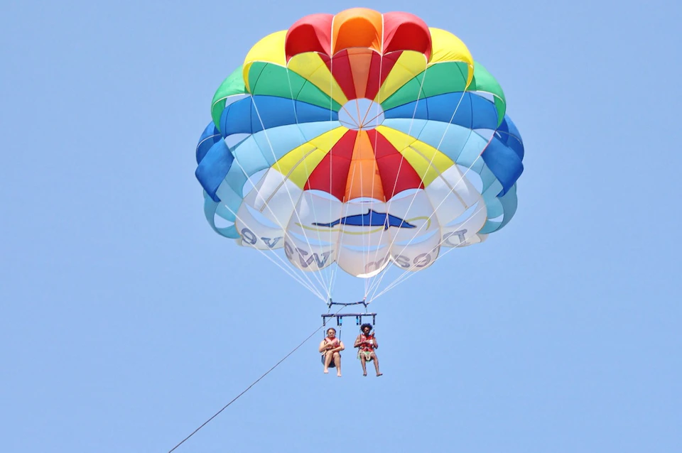 Two people parasailing with a colorful parachute against a clear blue sky.
