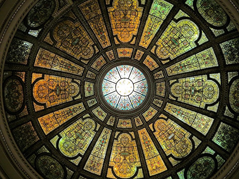 A large, ornate stained glass dome with intricate patterns and vibrant colors, viewed from below.