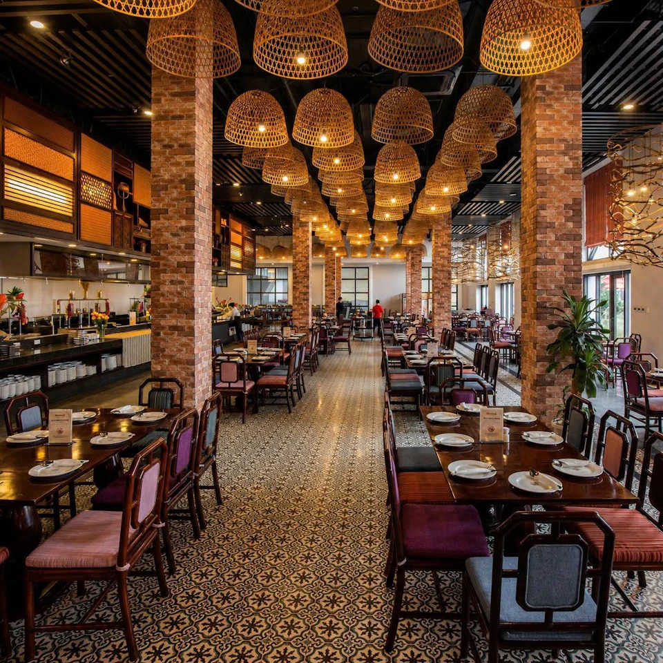 A spacious restaurant with brick columns, patterned floor, hanging lights, and neatly arranged tables with place settings.
