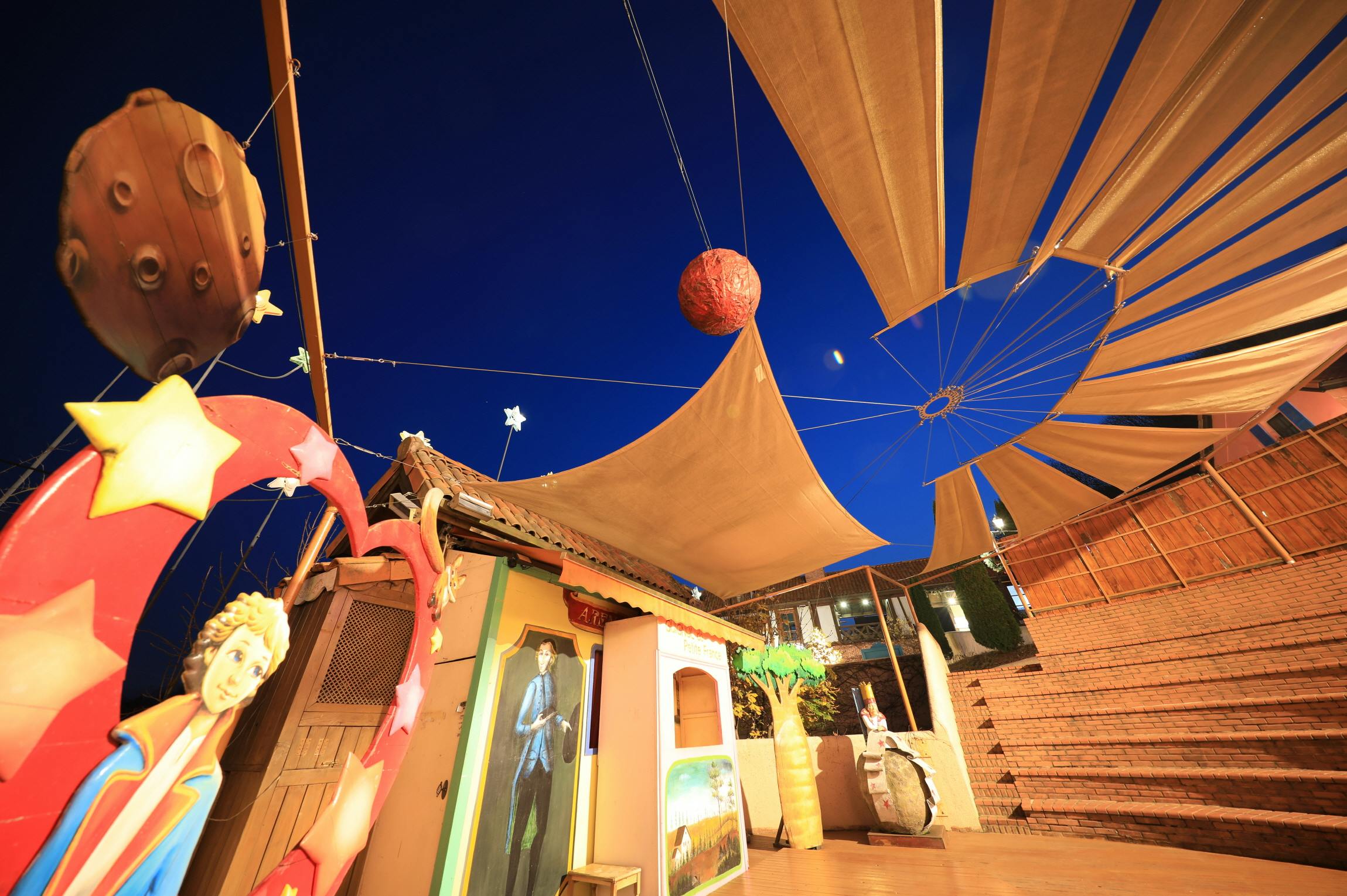 A vibrant outdoor scene with decorations of planets, stars, and colorful murals under a deep blue evening sky.