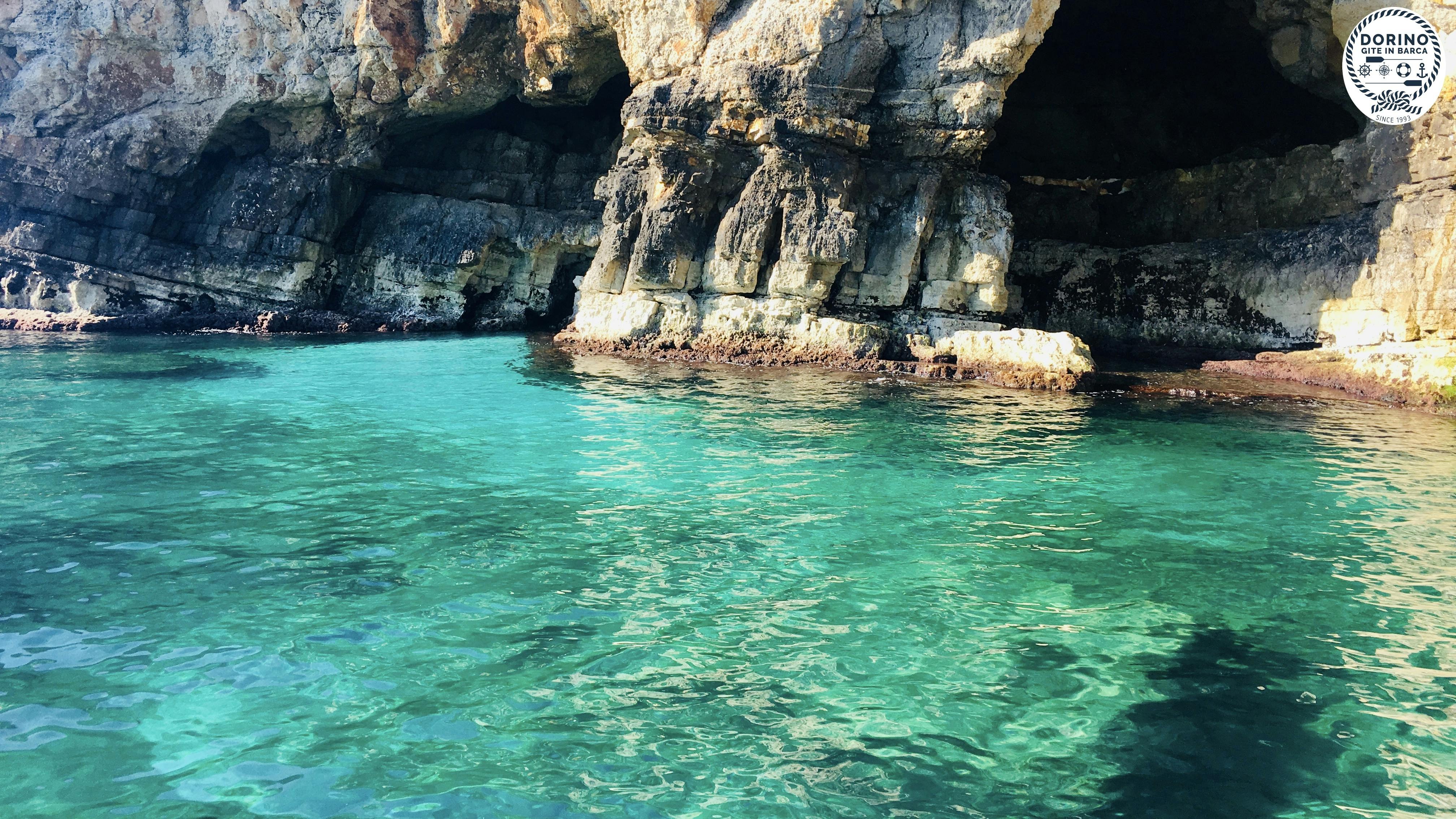 Una scogliera rocciosa con una grotta scura che si apre su un'acqua limpida e turchese.