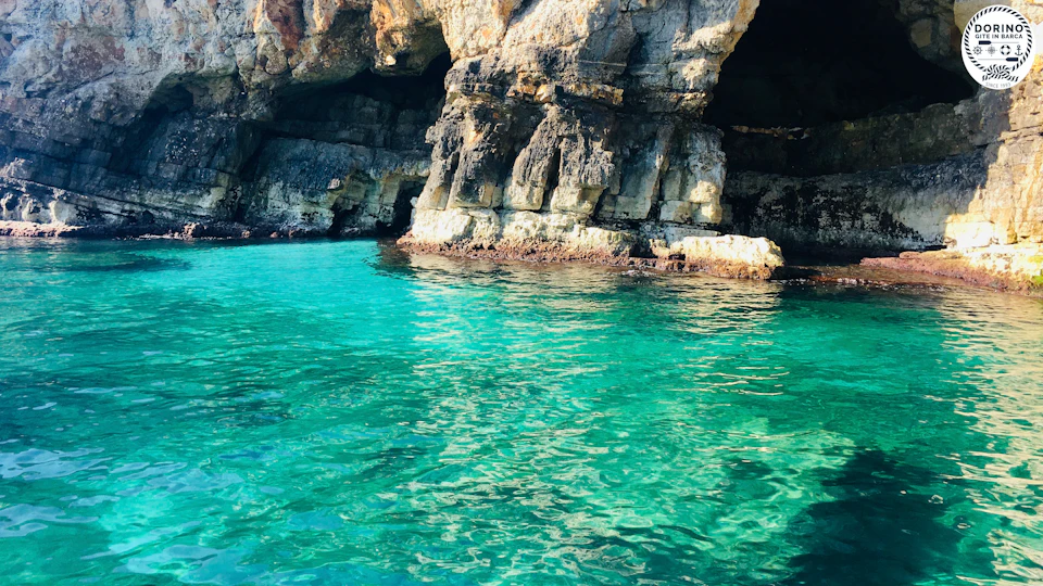 A rocky cliffside with a dark cave opening above clear turquoise water.
