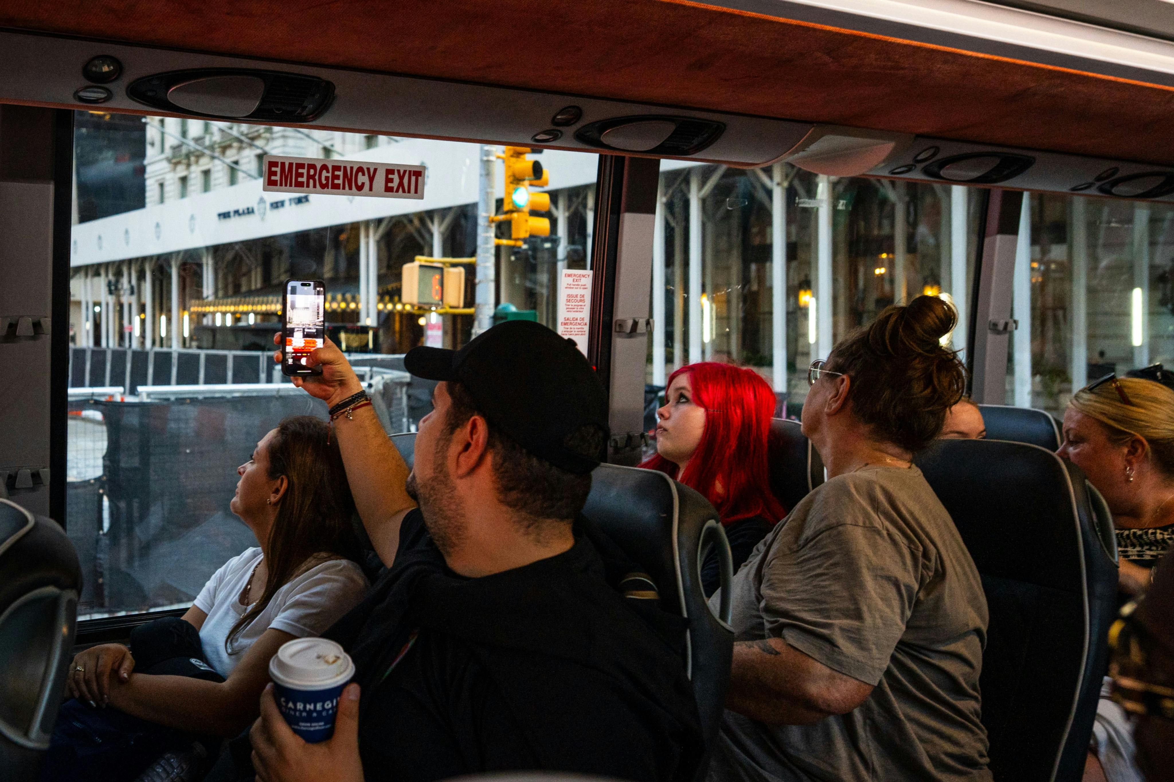 버스 안에서 사람들이 창문을 통해 사진을 찍고 있습니다. 비상구 표지판이 보이고 도시 거리가 바깥에 있습니다.