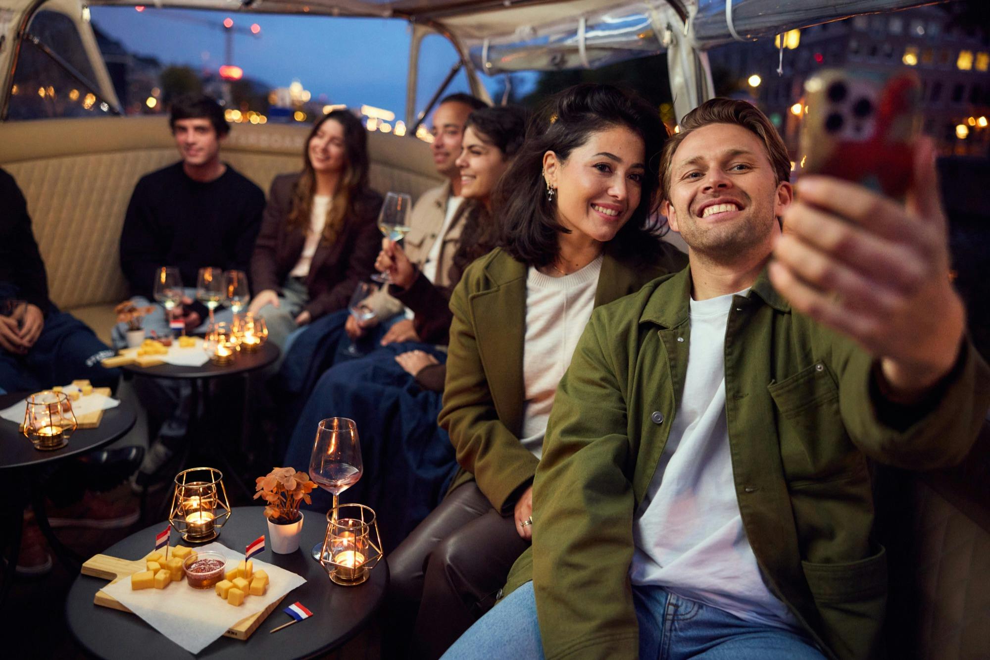 Um grupo de pessoas sentadas juntas num barco, com uma pessoa a tirar uma selfie e outras a segurar copos e a sorrir.