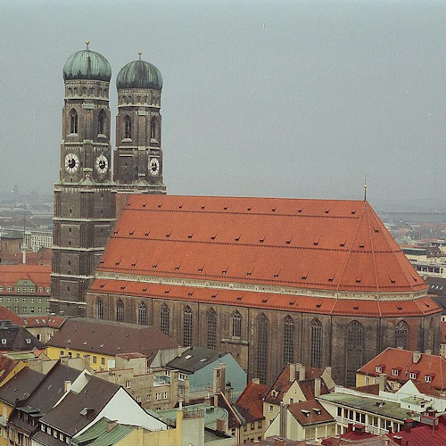 Luftaufnahme einer Stadt mit einer großen Kirche mit Zwillingstürmen und roten Dächern, umgeben von verschiedenen bunten Gebäuden.