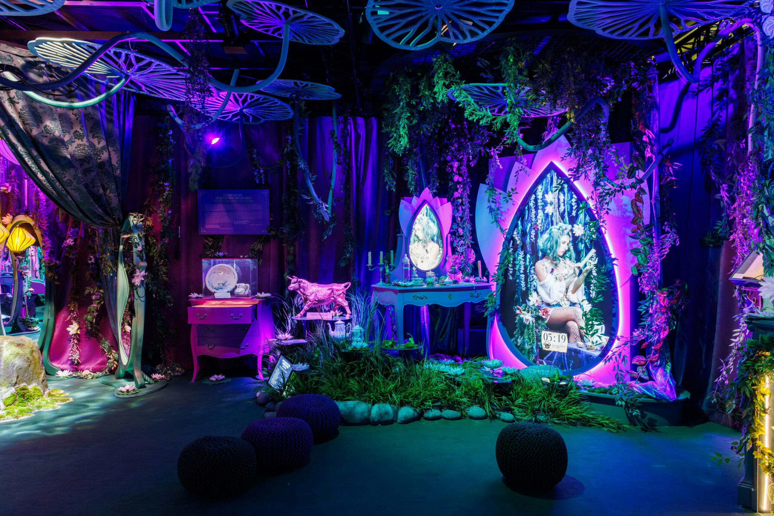 A whimsical, dimly lit room with a fantasy theme, featuring glowing purple decor, plants, and fairy-like imagery on mirrors and screens.