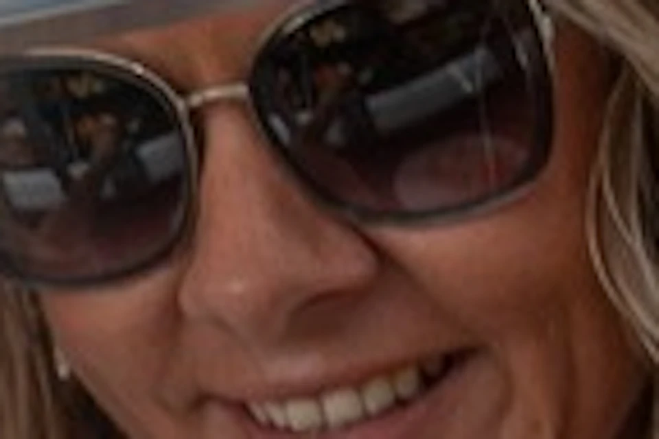 A smiling woman in sunglasses serves herself from a salad bar, with various fresh vegetables visible in the trays.
