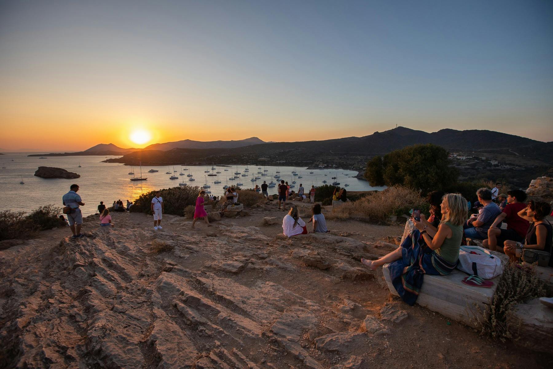 Visitors watching the sun set over the sea and anchored boats from Cape Sounion, a magical coastal view.