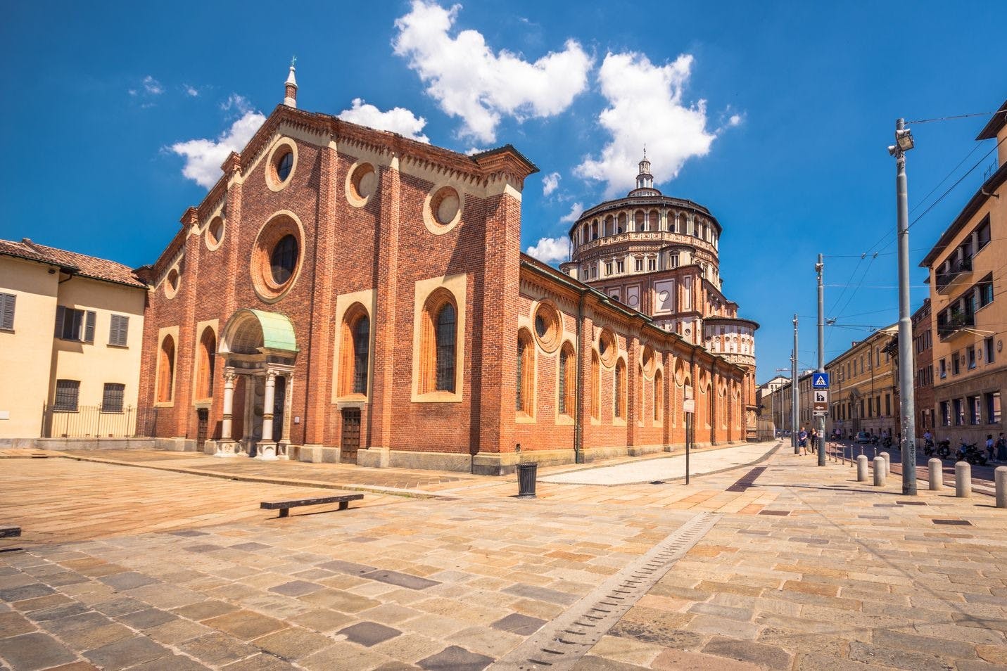 A historic brick building with round windows under a blue sky with clouds, featuring a domed structure in the background.