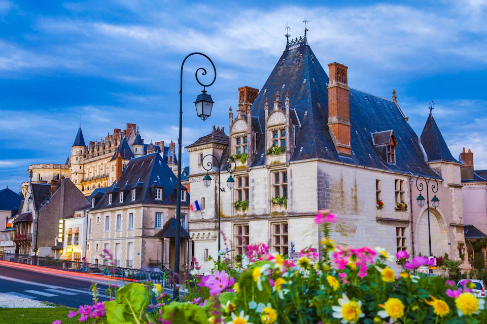 European-style buildings with steep roofs and chimneys, surrounded by colorful flowers and a vintage streetlamp in the foreground.