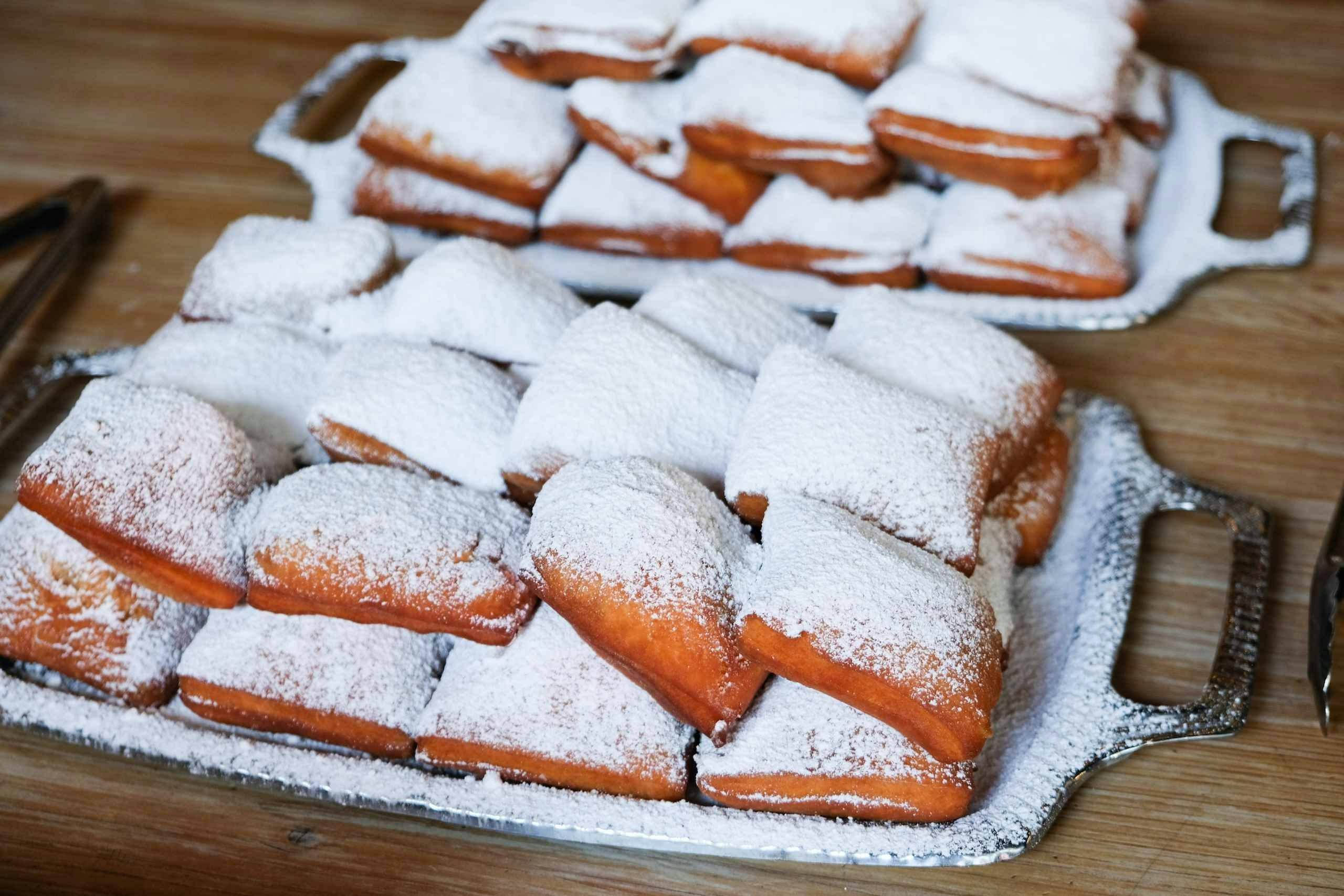 Vassoi di beignets appena fatti spolverati di zucchero a velo su un tavolo di legno.